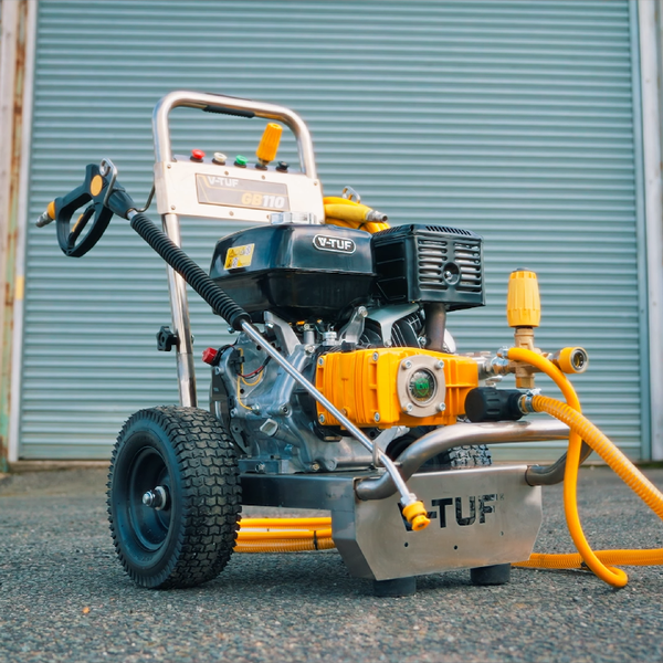 A TUF 12000 PSI portable gasoline pressure washer with a yellow and silver engine, black wheels, and a yellow hose, positioned outdoors in front of a gray metal garage door.